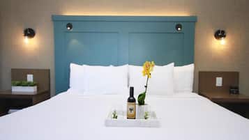 Quarto de hotel com uma cama grande, duas mesas de cabeceira, um criado-mudo, um relógio de parede e um aplique.