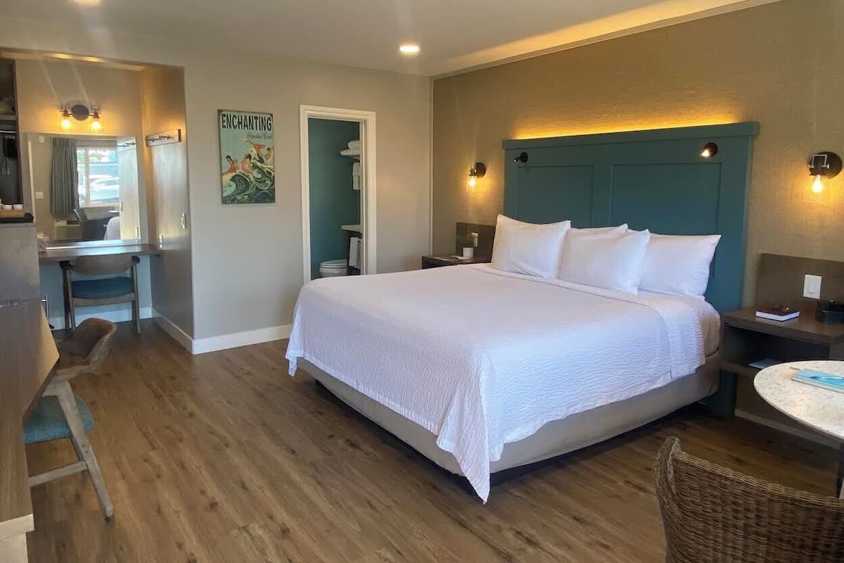 A bedroom with a bed, bedside tables, a chair, a small table, and a bathroom visible through an open door.