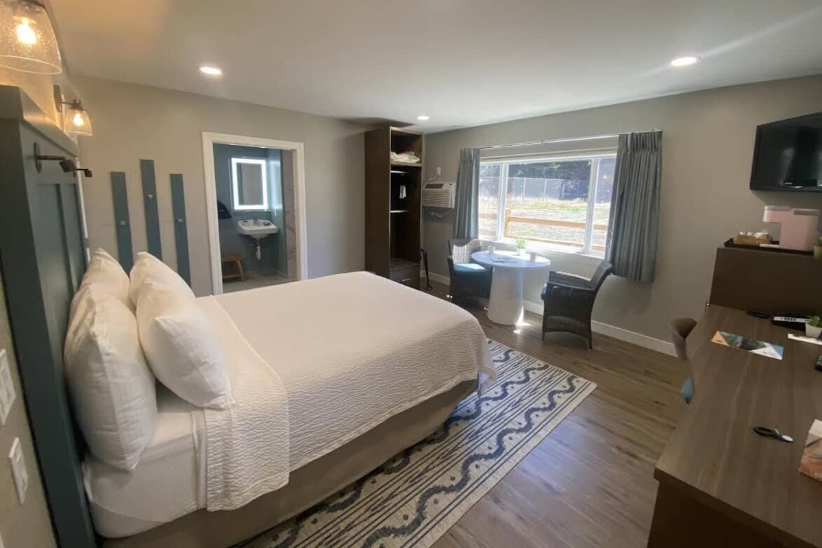 A bedroom with a bed, bedside table, TV, and a window with curtains.