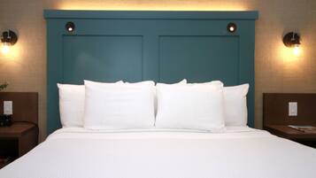 A neatly made bed with white linens and a teal headboard. There are two bedside tables with lamps and a small plant on one.