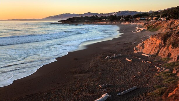A beach with waves, a clear sky, and birds flying. - Castle Inn (Cambria)