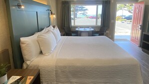 A hotel room with a large bed, a small table with two chairs, a window with curtains, and a door with a number. - Castle Inn (Cambria)