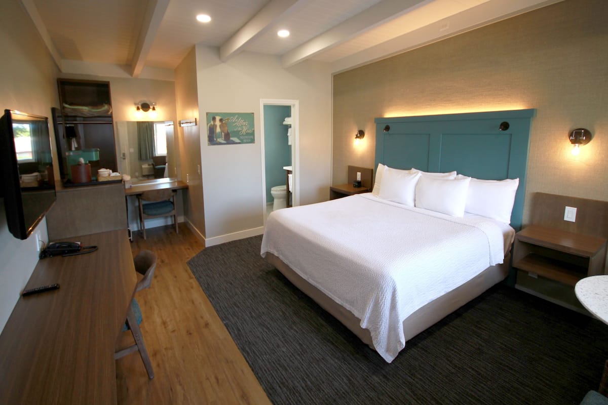 A hotel room with a large bed, a desk, a chair, a mirror, and a small table.
