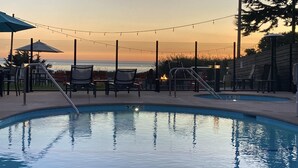 A pool area with lounge chairs and a view of the ocean at sunset. - Castle Inn (Cambria)