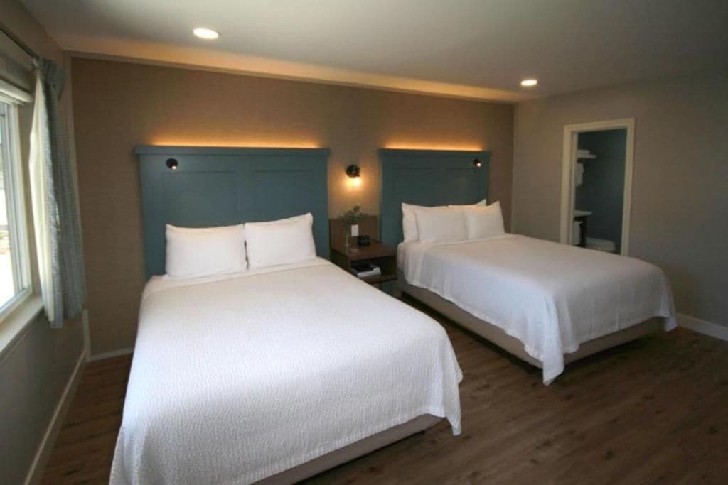 Habitación de hotel con dos camas, suelo de madera y una mesita de noche con lámpara.