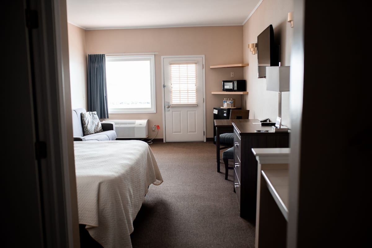 A hotel room with a bed, a desk, a chair, a microwave, and a television.