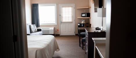 Habitación de hotel con cama, escritorio, silla, microondas y televisor.