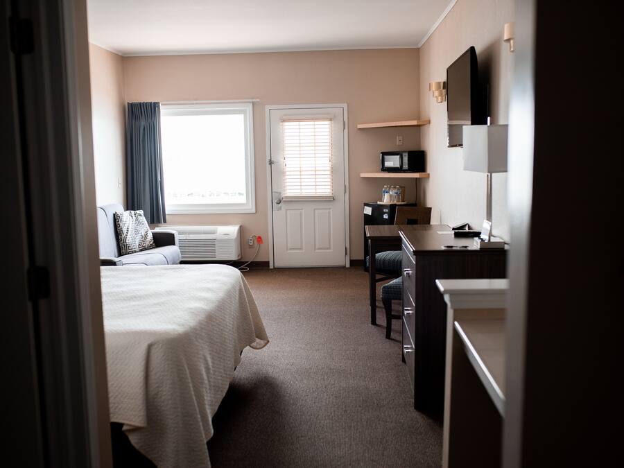 A hotel room with a bed, a desk, a chair, a microwave, and a television.