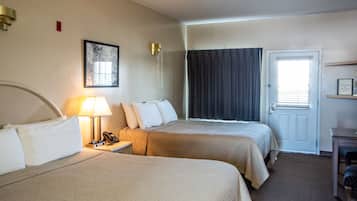 A hotel room with two beds, a bedside table with a lamp, a telephone, a door with a window, and a small table with a chair.