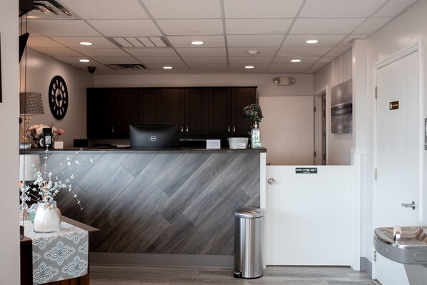 A modern reception area with a herringbone-patterned wall, a reception desk, a clock, and a trash bin. - West Bank Inn (Celina)