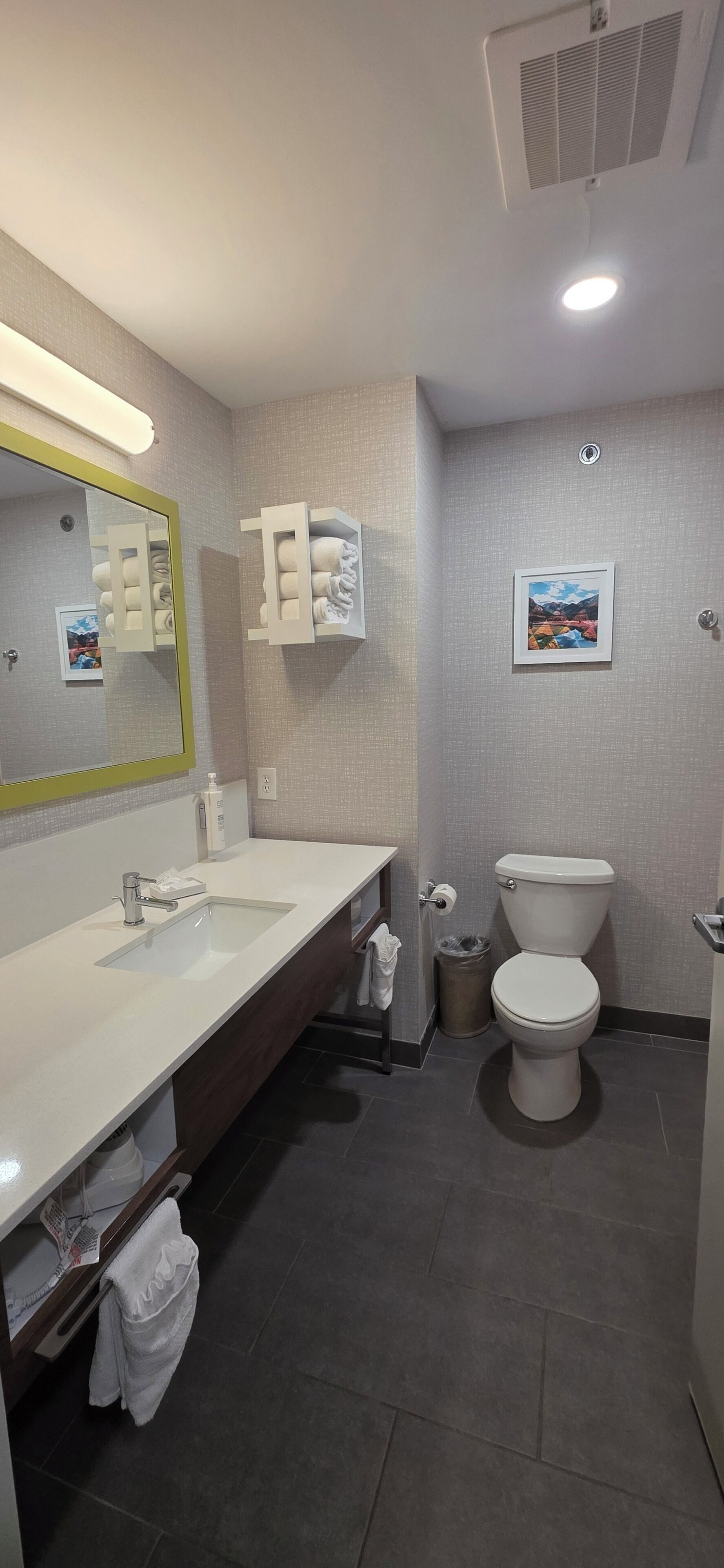 A modern bathroom with a white sink, mirror, and toilet. There are towel racks and a trash can.