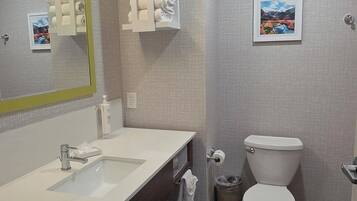 A modern bathroom with a white sink, mirror, and toilet. There are towel racks and a trash can.