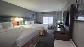 Habitación de hotel con dos camas, un escritorio, un televisor y una ventana con persianas.