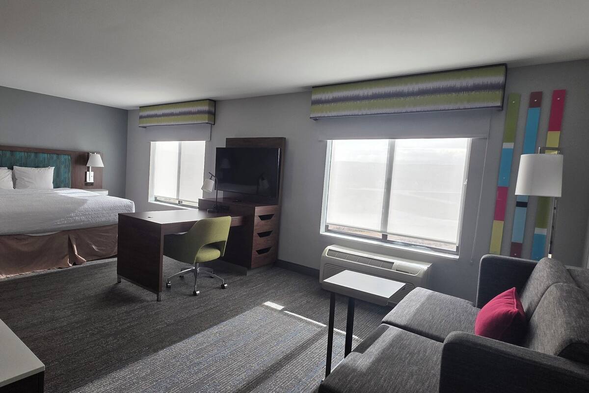 A hotel room with a bed, desk, chair, TV, and a couch.