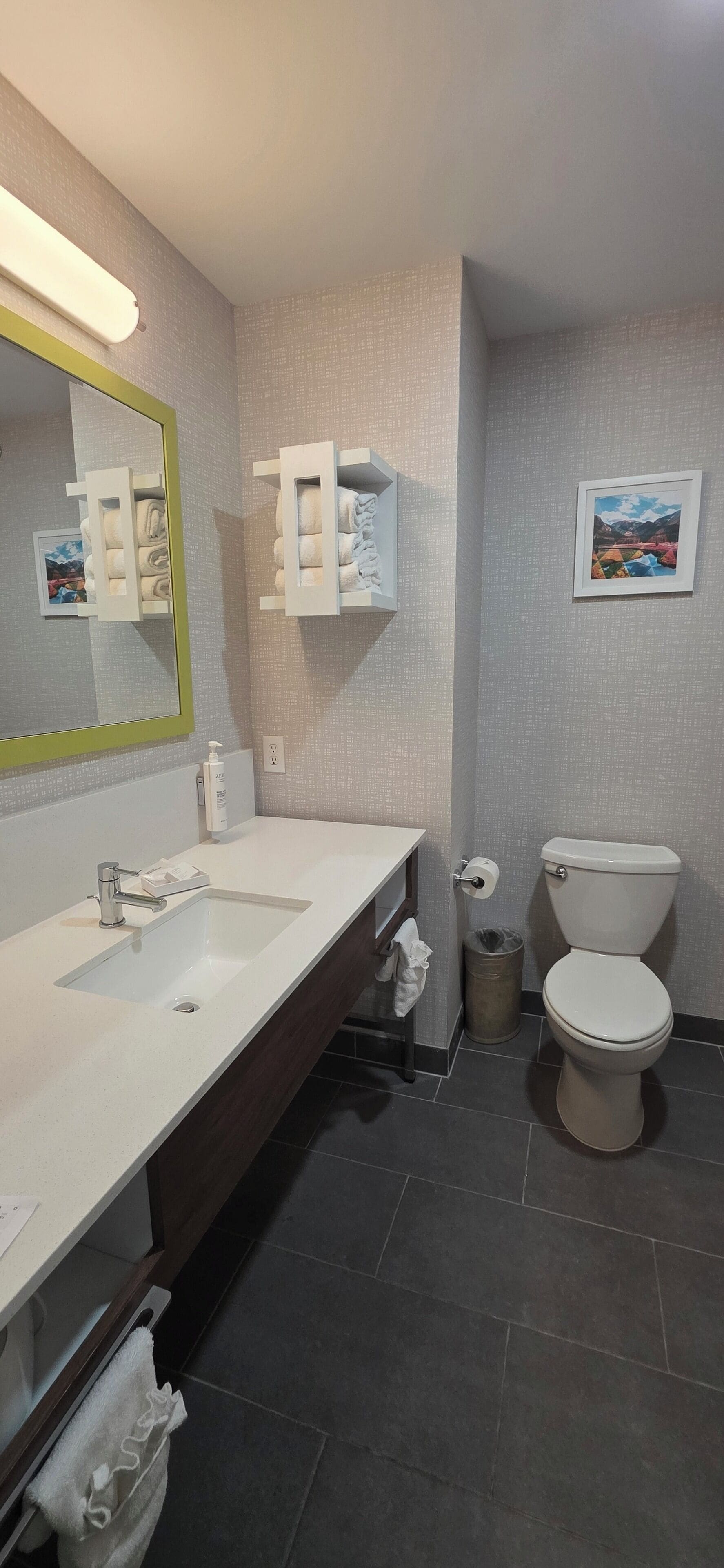 A modern bathroom with a white sink, mirror, and toilet. There are towel racks and a trash can.