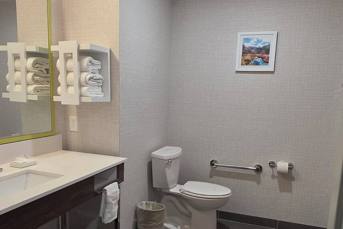A modern bathroom with a large mirror, white sink, and toilet.
