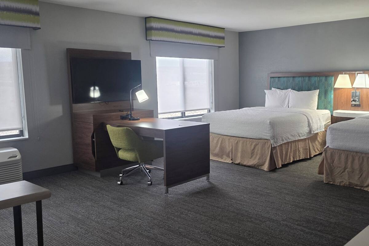 A hotel room with two beds, a desk, a chair, a TV, and a telephone.