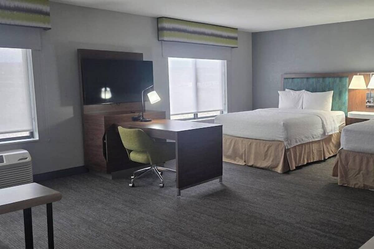 A hotel room with two beds, a desk, a chair, a TV, and a window.