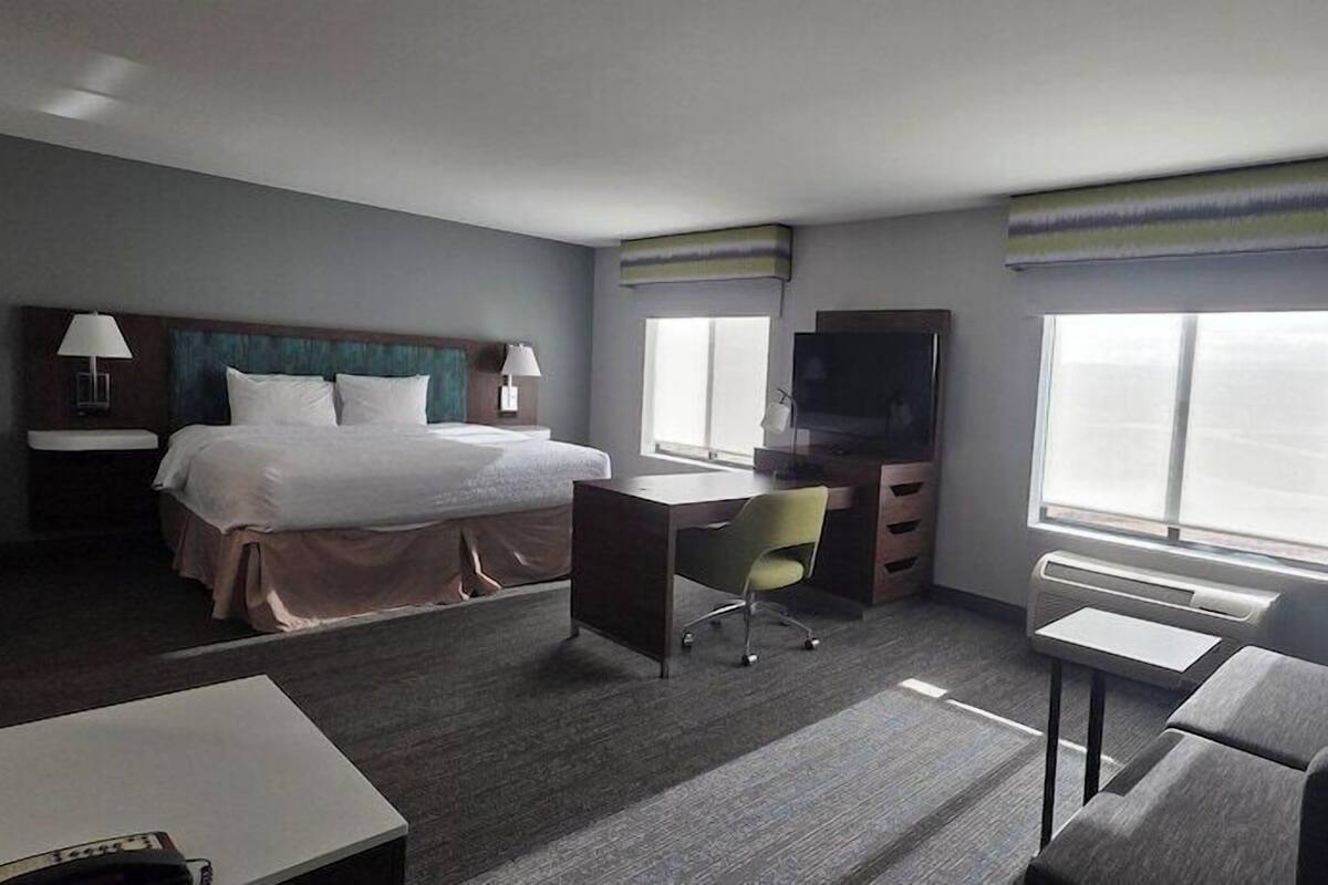 A hotel room with a bed, desk, chair, TV, and a sofa.