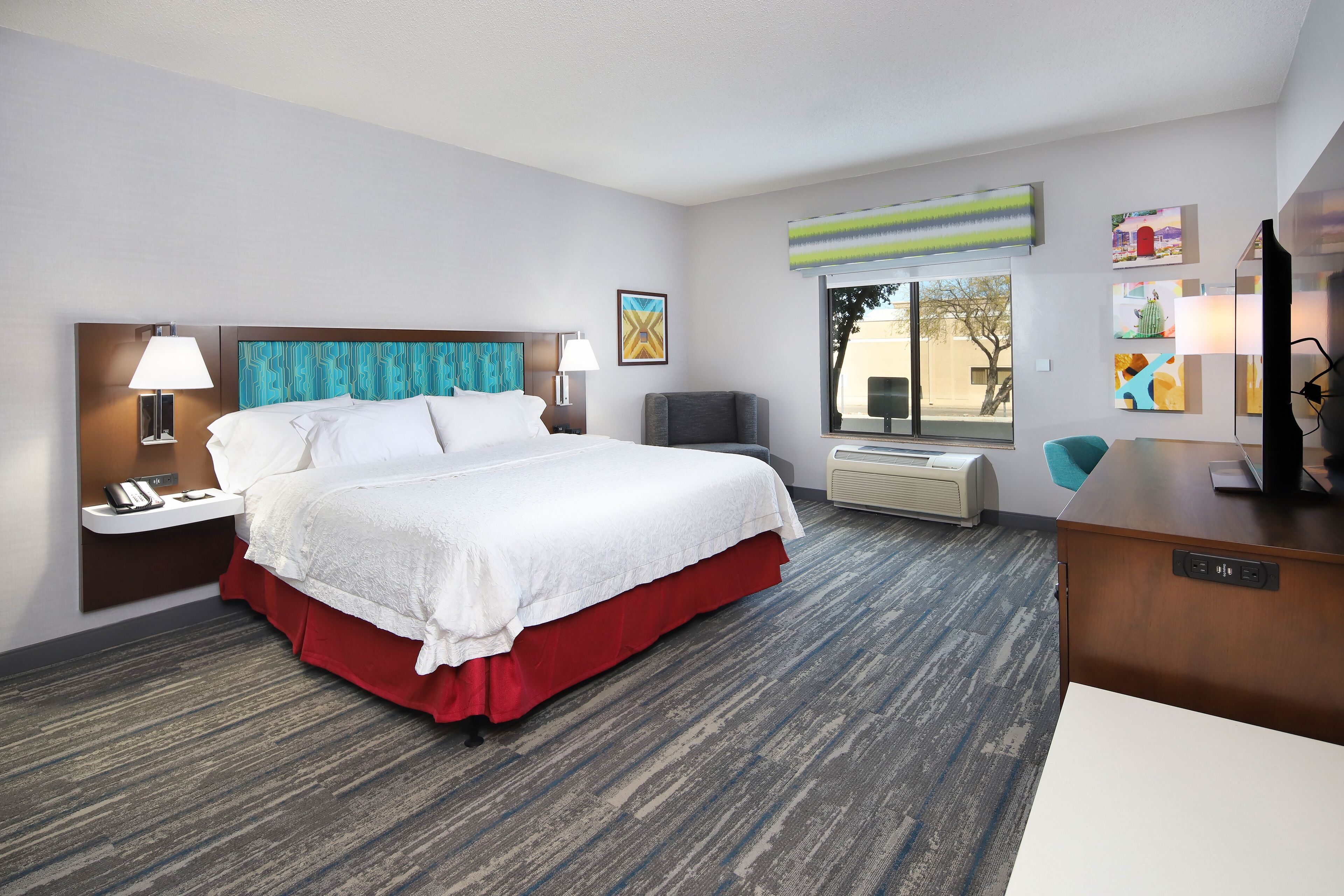 A hotel room with a large bed, a desk, a chair, a TV, and a window with a view of the outside.