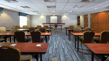 Un salón de conferencias con varias mesas y sillas, una pantalla de proyección grande y suelo alfombrado.