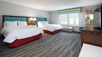 A hotel room with two beds, a desk, a television, and a window with blinds.