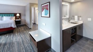 A hotel room with a bed, bedside table, lamp, framed artwork, and a bathroom with a sink, mirror, and towel rack. - Hampton Inn & Suites Tucson East/Williams Center (Tucson)