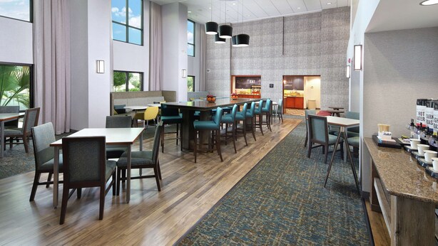 A modern hotel lobby with a long dining table, multiple chairs, a coffee bar, and large windows. - Hampton Inn & Suites Tucson East/Williams Center (Tucson)