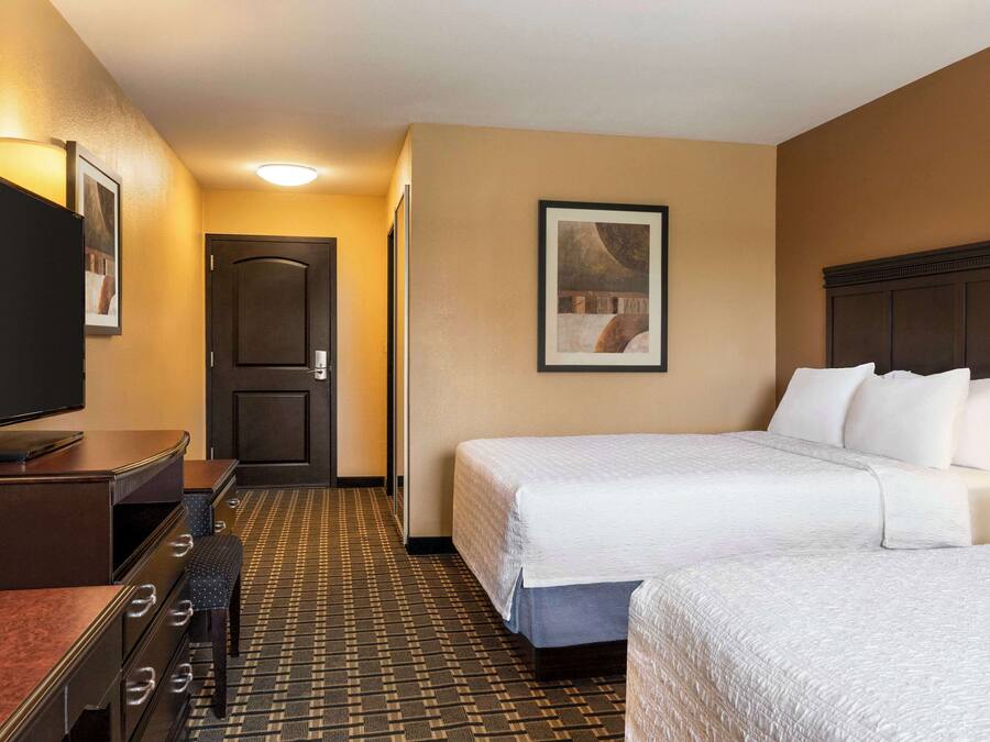 Een hotelkamer met twee bedden, een bureau, een televisie en een ingelijst foto aan de muur.