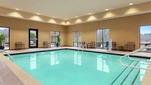 Une piscine intérieure à l’eau d’un bleu cristallin, entourée de murs de couleur beige et dotée de grandes fenêtres.