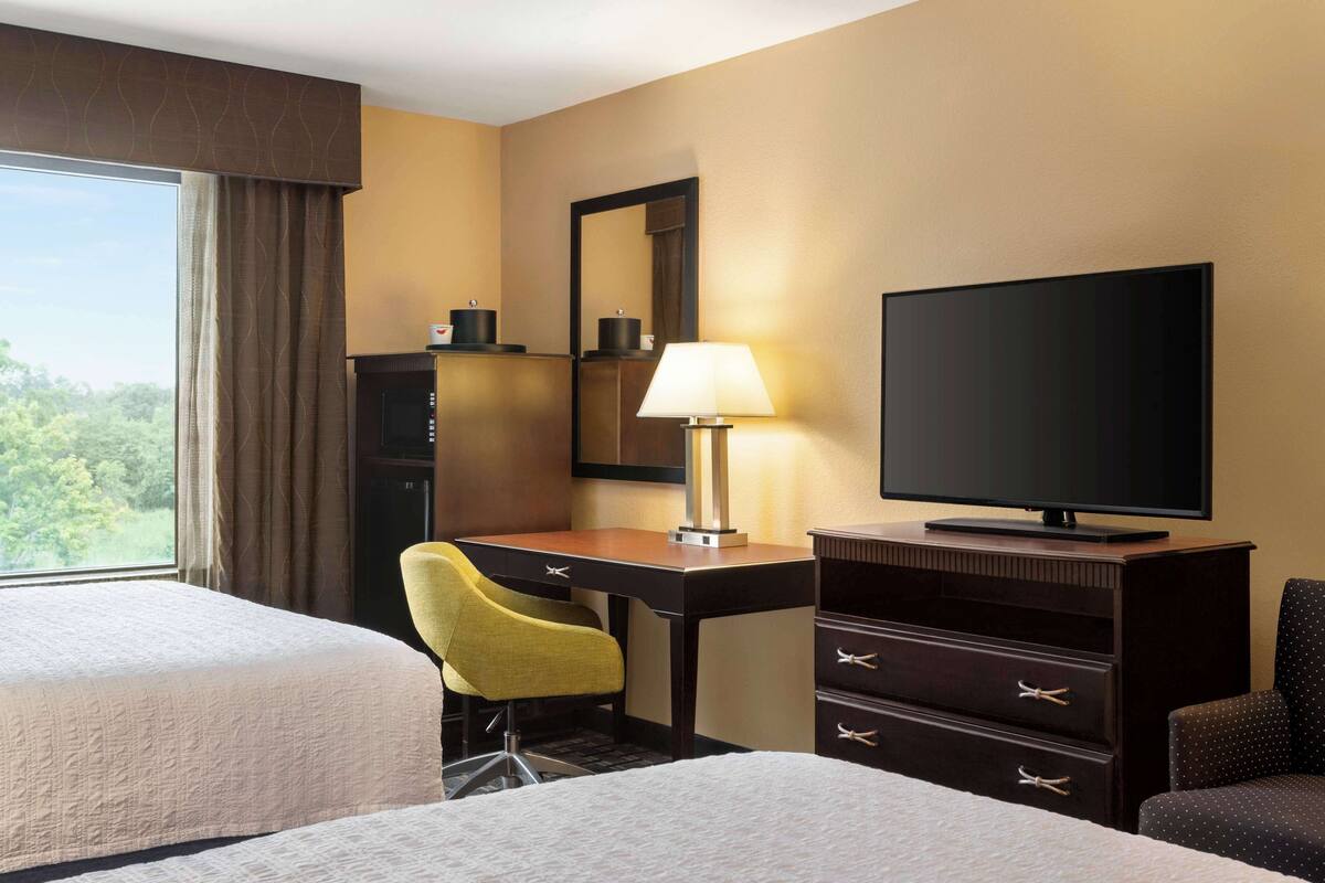 Quarto de hotel com duas camas, uma escrivaninha com cadeira, televisão e cómoda.