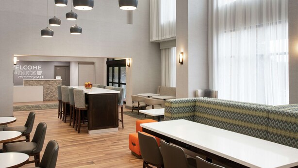 Un hall d’hôtel moderne doté d’un comptoir d’accueil, de plusieurs espaces salon et de grandes fenêtres.