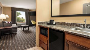 Une chambre d’hôtel compacte dotée d’une kitchenette, d’un coin salon avec un canapé et un fauteuil, d’un grand miroir et offrant une vue sur l’extérieur.