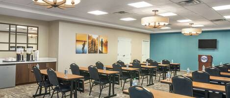 A conference room with multiple tables and chairs, a kitchenette, and a large screen.