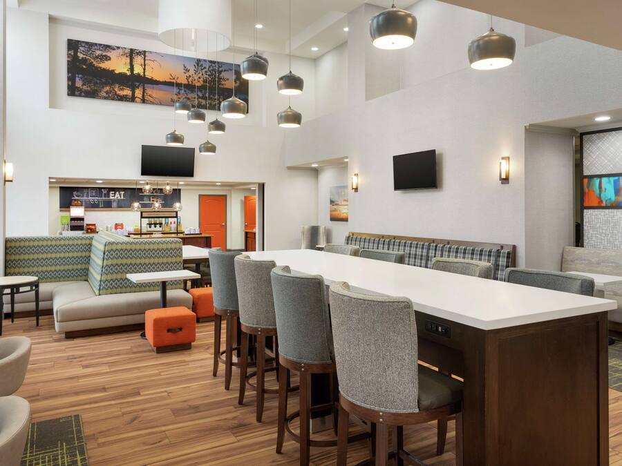 Un hall d’hôtel moderne doté d’une longue table commune, d’un bar, de coins salon et d’un écran de télévision.