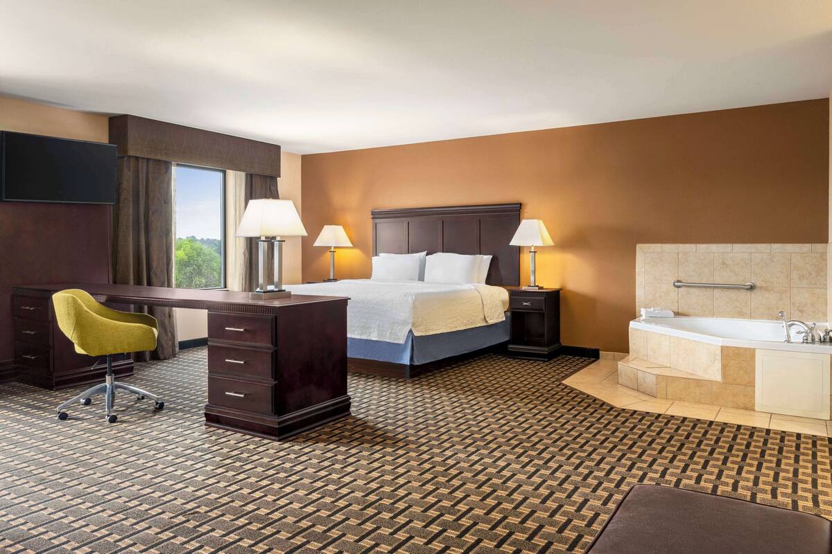 Quarto de hotel com cama, escrivaninha, cadeira, luminárias e banheira.