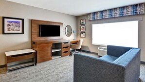 A hotel room with a wooden desk, a television, a blue couch, and a large window. - Hampton Inn by Hilton Moab (Moab)