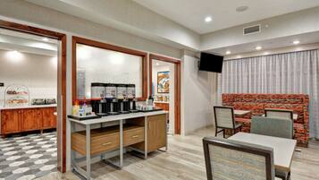 Una habitación de hotel moderna con kitchenette, un comedor con mesa y sillas, y una zona de estar con sofá estampado.