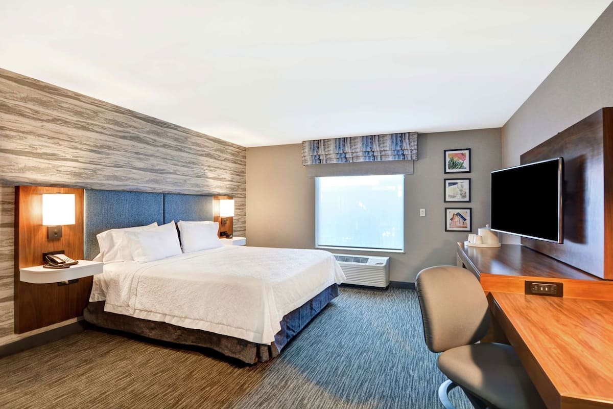 A hotel room with a bed, bedside table with a phone, a desk with a TV, and a window with a view.