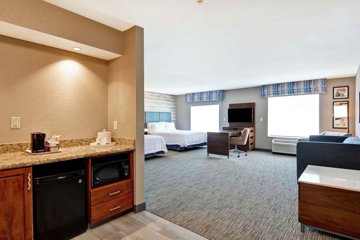A hotel room with a kitchenette, a bed, a desk, and a TV.
