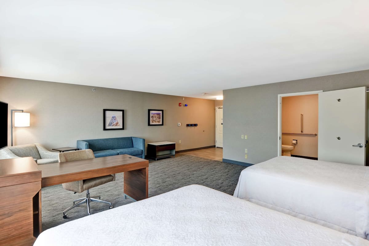 A hotel room with a bed, a desk, a chair, a sofa, and a television.
