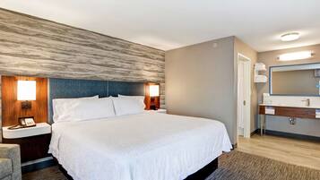 A hotel room with a large bed, bedside tables with lamps, a wooden headboard, a bathroom with a mirror, and a wooden floor.