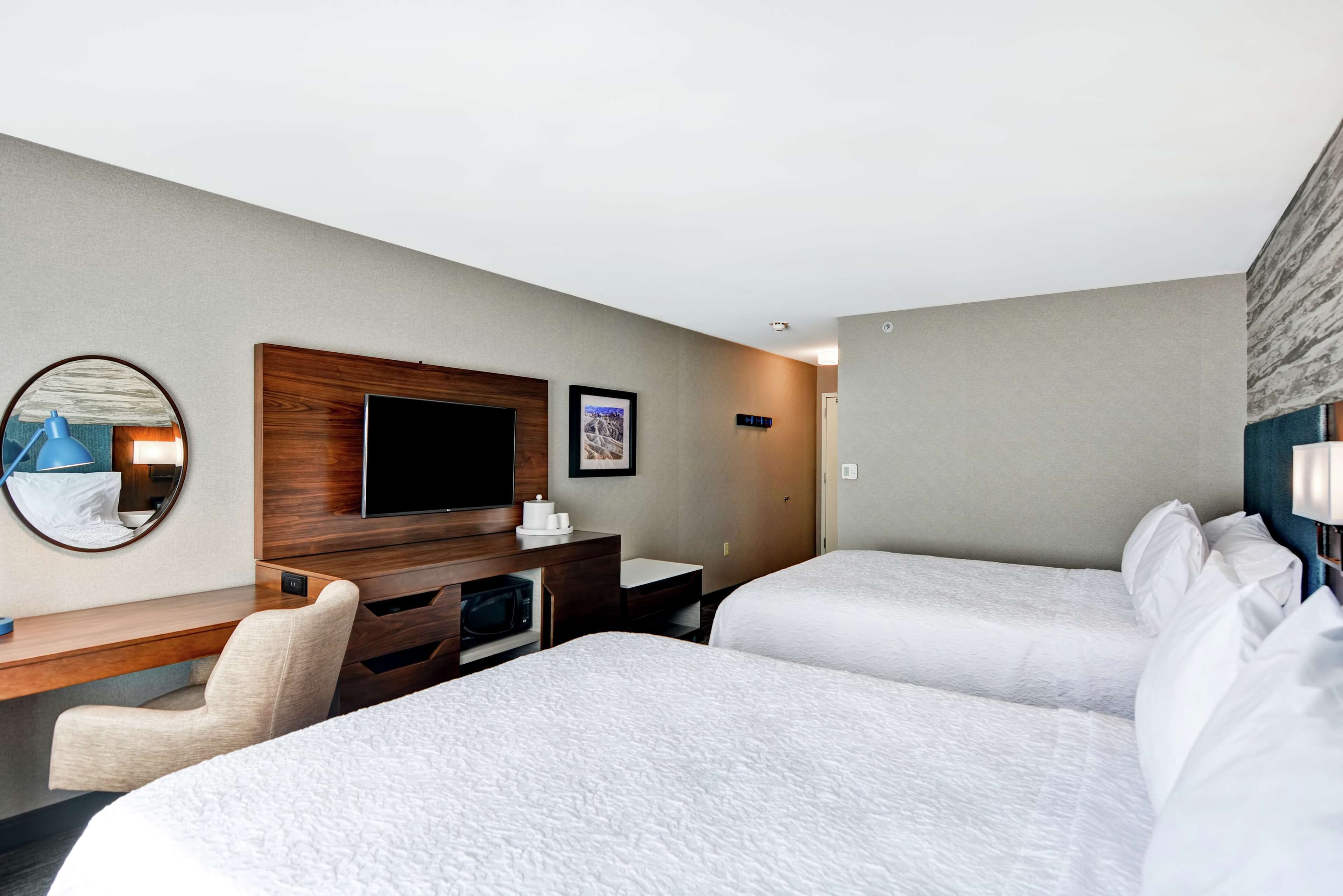 A hotel room with two beds, a desk, a TV, and a mirror.