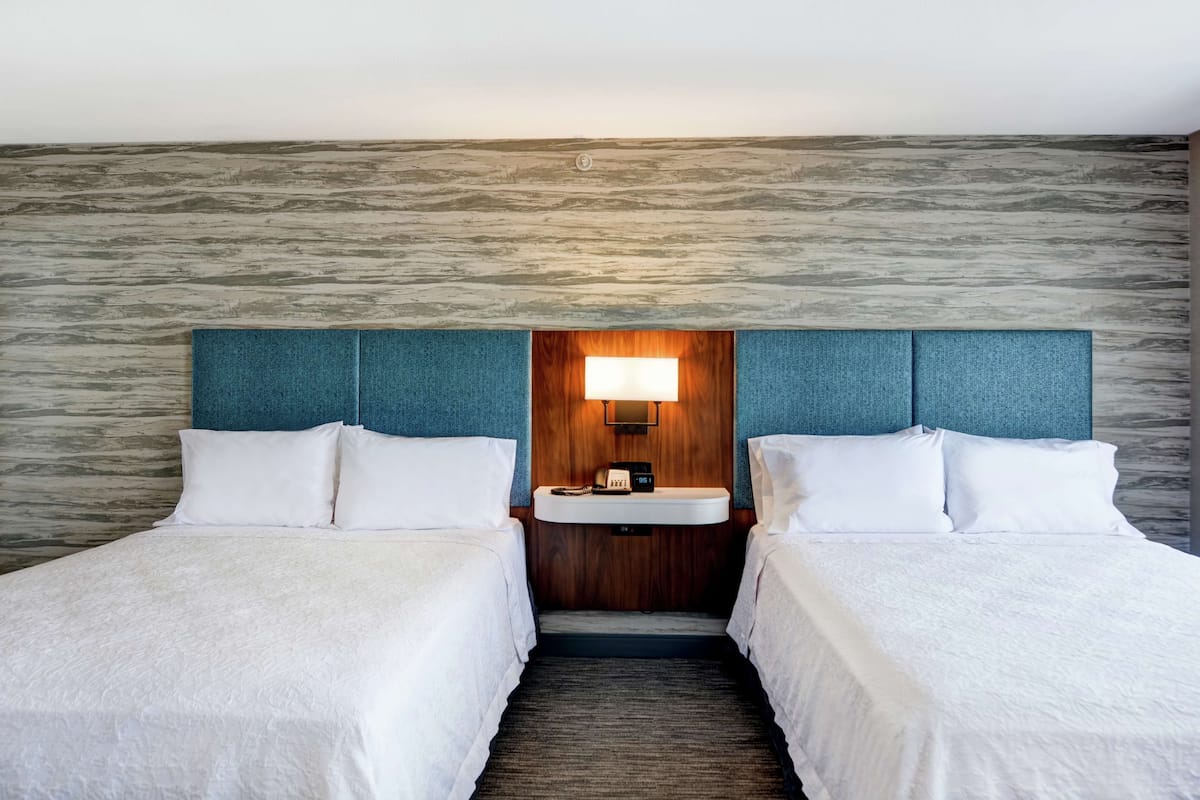 A hotel room with two beds, a wooden headboard, a built-in sink, and a textured wall.
