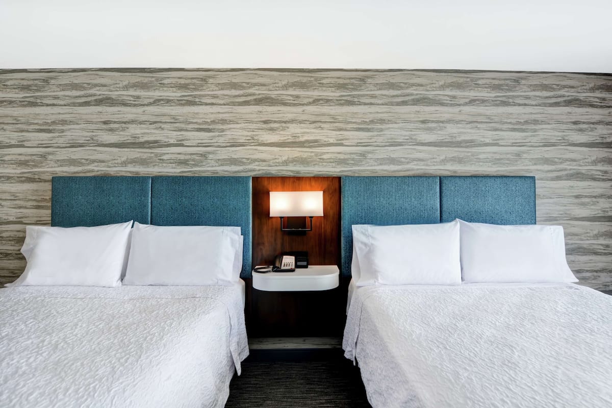 A hotel room with two beds, a built-in sink, and a wooden headboard.