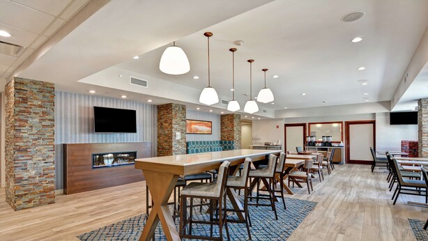 A spacious hotel lobby with a long wooden reception desk, multiple seating areas, a fireplace, and a television mounted on the wall. - Hampton Inn by Hilton Moab (Moab)