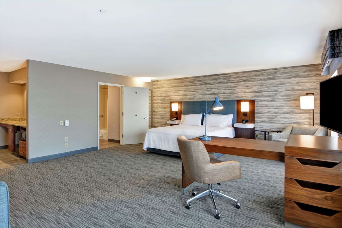 A hotel room with a bed, desk, chair, and a television.