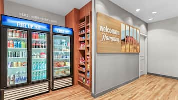 A hotel lobby with a 'Welcome to Hampton' sign, a 'Fuel Up Here' refrigerated display, and a 'Chill Out' refrigerated display.