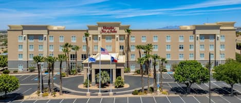 A hotel with a central entrance, palm trees, and a parking lot.