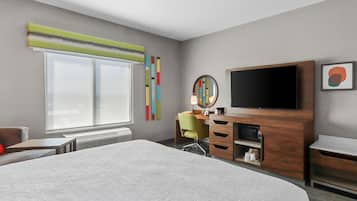 A hotel room with a large bed, a desk with a chair, a television, and a window with blinds.